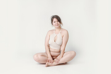 Obraz premium A plump woman with a hairstyle, smiling at the camera, sitting in the studio in her underwear. A bodypositive large-sized woman who feels comfortable in her natural body.