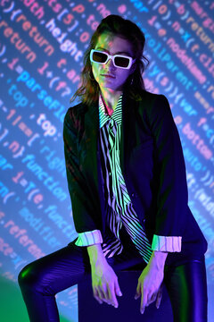 Woman in sunglasses sitting in room with neon illumination