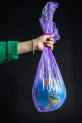 Female hand holding plastic bag with world globe. Isolated on black background.