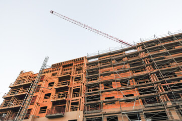 Multi-story wood-frame building under construction with scaffolding and overhead tower crane, illustrating residential or mixed-use development and structural framing processes