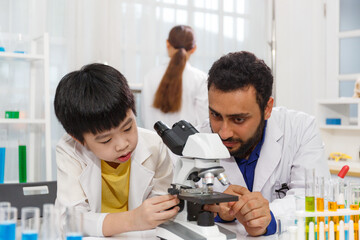 male teacher sitting at classroom desk with male student using microscope while learning science experiment