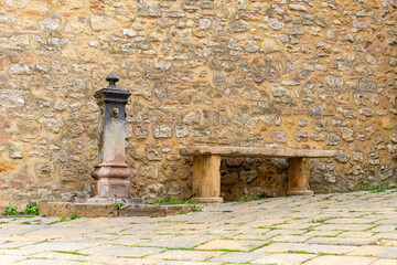 Source of water in a lane of historic Tuscan town with stone bench and a beautiful wall with stone...