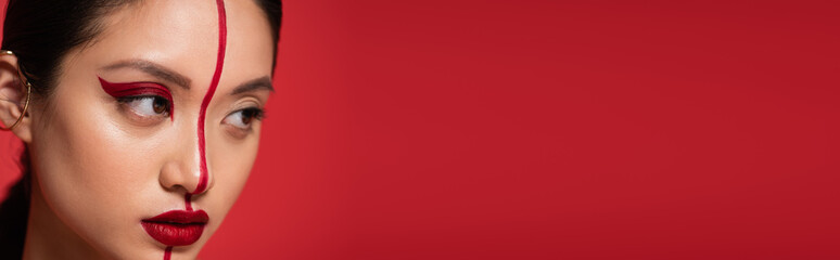 portrait of young asian model with artistic makeup and perfect skin looking away isolated on red, banner.