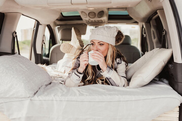 Woman holding a mug with hot drink laying down on bed in camper van.Camping lifestyle and relax
