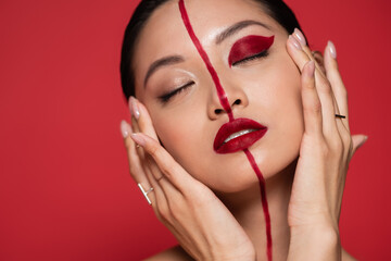 portrait of sensual asian woman touching perfect face with bright artistic makeup while posing with...