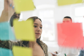 Diverse colleagues working on startup with sticky notes on glass board