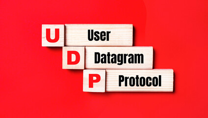 On a bright red background, wooden cubes and blocks with the text UDP User Datagram Protocol. Manufacturing of wooden toys.