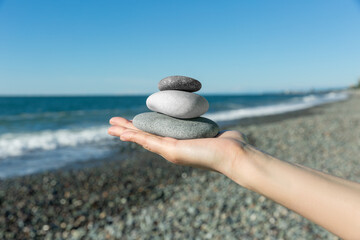 Balance of stones on the hand against the background of the sea. The concept of peace of mind, harmony, spirituality