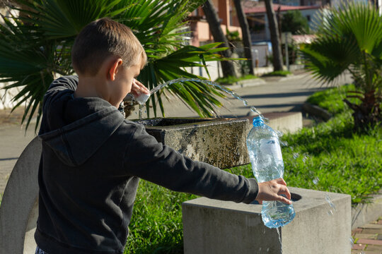 Funny little boy filling his water bottle in public fountain
