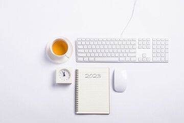 Conceptual,mouse and keyboard with clock and tea on white blackground work space.open diary with blank space for new year's resolutions 2023.
