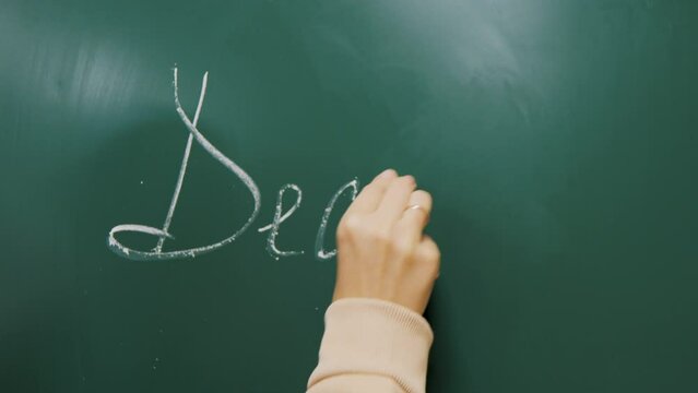 hand writing on a blackboard. the teacher writes on the green board in the classroom. educational process at school. writes with chalk on the board.