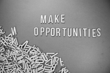 MAKE OPPORTUNITIES in wooden English words language capital letters spilling from a pile of letters on a blue background - black and white