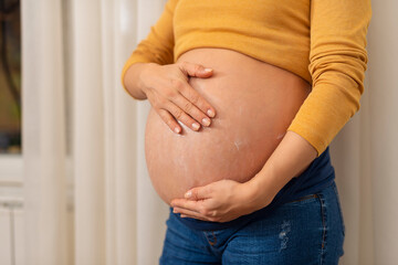 Pregnant Woman holding and stroking apply cream on big belly for beauty moisturizing skin at home