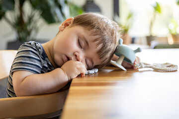 Tired child sleeping highchair on dining table after lunch