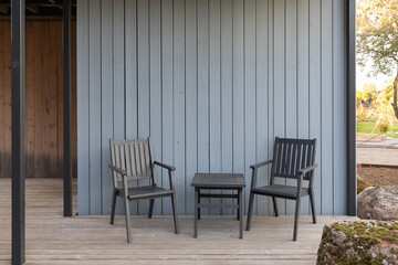 Wooden terrace of a Scandinavian-style country house with wooden furniture - chairs and a table