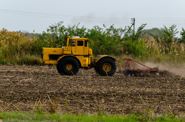 Obraz premium The tractor prepares the land with the help of a cultivator for pre-sowing work, on rice checks. Cultivated field Agronomy farming concept