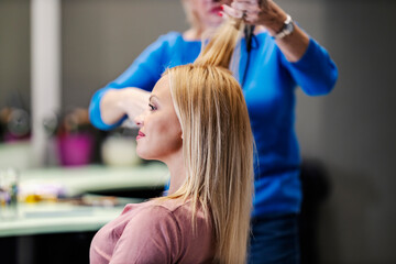 Fototapeta premium A happy customer is sitting in hair salon while hair stylist is styling her hair.