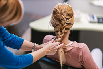 A hairdresser is making braid in a salon. - obrazy, fototapety, plakaty