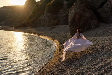 A mysterious female silhouette with long braids stands on the sea beach with mountain views, Sunset...