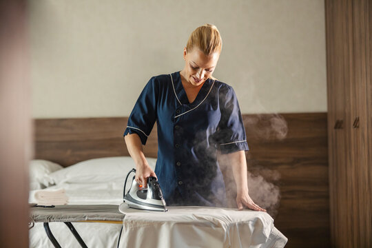 A maid is ironing shirt in a hotel room.