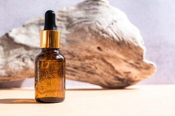 Amber glass dropper bottle with cosmetic liquid and natural wood on beige background. Side view, space for text.