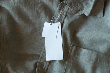 Blank price label tag paper card on gray natural linen shirt. Clothes label tag mockup template...