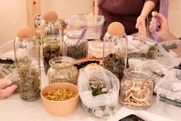 Herbal tea collection. Glass jars with lids. Master class on cooking, training. The hands of the participants are large against the background of jars and bowls with herbs. Ecological, clean.