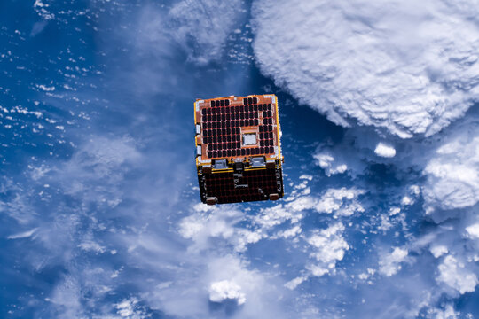Small squared Satellite orbiting in outer space above planet earth deployed by the international space station. Picking up space debris. Digitally enhanced. Elements of this image furnished by NASA.