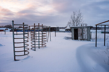 Abandoned playground and outdoor toilet covered with snow