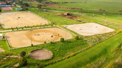 Fototapeta na wymiar Aerial view of three horsemen. A riding field with fence and obstacles to train horses. In this sports facility, tournaments and horse racing courses are organized. The sports center is in the nature.