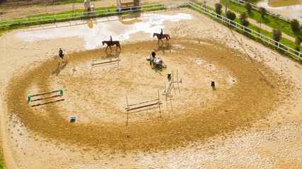 Aerial view of three horsemen. A riding field with fence and obstacles to train horses. In this...