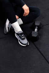 Fototapeta na wymiar equiped girl resting on the black floor after workout with barbell. Long legs with black pants and white socks. Copy free space