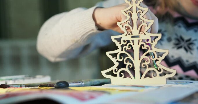 The holiday season. The hands of a small child coloring a toy wooden Christmas tree with a brush. Hand held. Close-up.