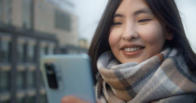 Young happy asian woman communicates by video call on the street. Close-up portrait of a girl with a smartphone on the background of the city. Autumn, urban landscape