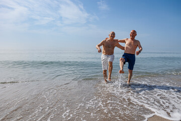coppia di anziani al mare giocano sula riva schizzando e calciando l''acqua - obrazy, fototapety, plakaty