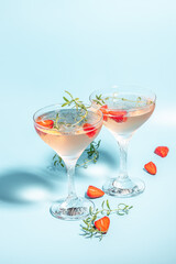 Glasses with cold pink champagne or punch with wine strawberries, ice and rosemary on blue background