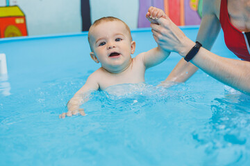 A swimming teacher teaches a little boy to swim in the pool. Children's first swimming lessons. Development for babies