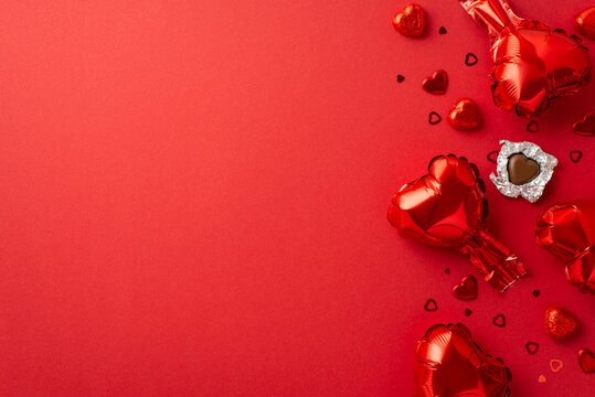 Saint Valentine's Day concept. Top view photo of heart shaped balloons unwrapped chocolate candies and confetti on isolated red background with empty space