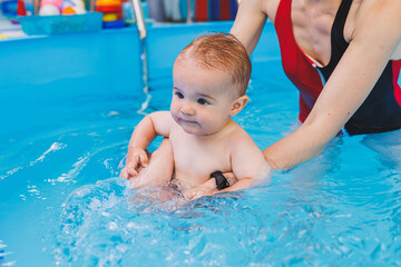 Fototapeta na wymiar A beautiful mother teaches teaches her little son how to swim in the pool. A child is having fun in the water with his mother. Child development. First swimming lessons for children