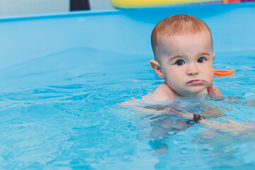 Fototapeta na wymiar A little boy is learning to swim in a baby pool. Children's development. First swimming lessons for children