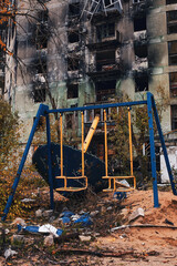 Playground after artillery shelling, Children's swings with traces of shrapnel from the explosion. A playground on the background of a burned down house. Consequences of military operations