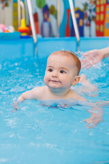 Fototapeta na wymiar Swimming lessons for children. A little boy is learning to swim in a baby pool. Children's development. First swimming lessons for children