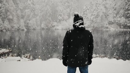 Back view of the man in warm winter clothes during the snowfall near lake Blausee in Swiss Alps. Steadicam tracking shot - Powered by Adobe