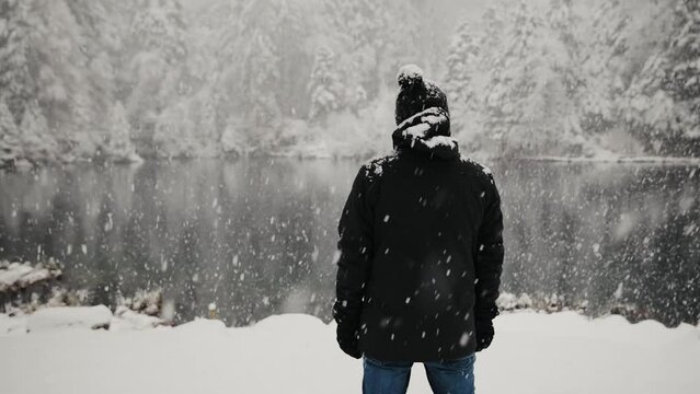 Back view of the man in warm winter clothes during the snowfall near lake Blausee in Swiss Alps. Steadicam tracking shot