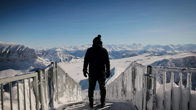 Unrecognizable man standing on the top of Glacier 3000 on Peak Walk bridge against beautiful winter mountains landscape. Back view steadicam shot. Swiss Alps