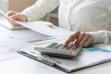 Account finance, analysis asian young business woman hand use calculator for calculate budget, cost and income of company from reports paperwork, plan spend money expenses, working on desk at home.