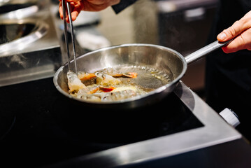 man chef cooking tasty shrimp in frying pan on kitchen
