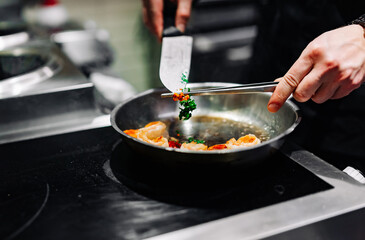 man chef cooking tasty shrimp in frying pan on kitchen
