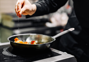 man chef cooking tasty shrimp in frying pan on kitchen
 - obrazy, fototapety, plakaty