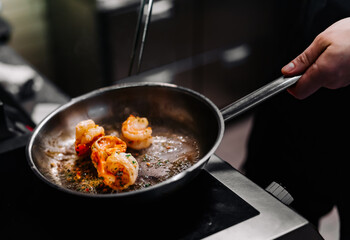 man chef cooking tasty shrimp in frying pan on kitchen

